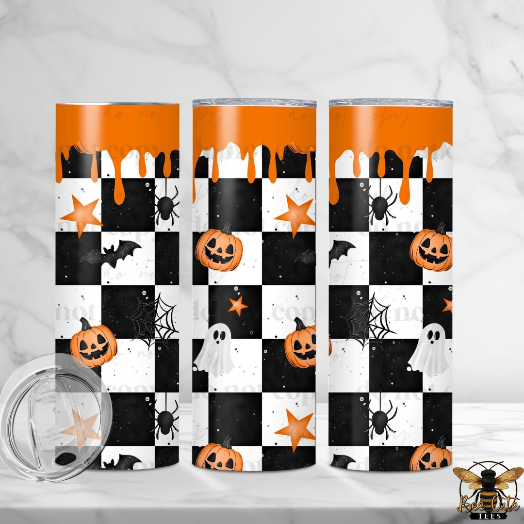 Three tall stainless steel tumblers with a Halloween-themed checkerboard wrap design, featuring orange pumpkins, ghosts, spiders, stars, and dripping orange graphics. A clear lid with a silicone seal is shown in the foreground on a white marble surface.