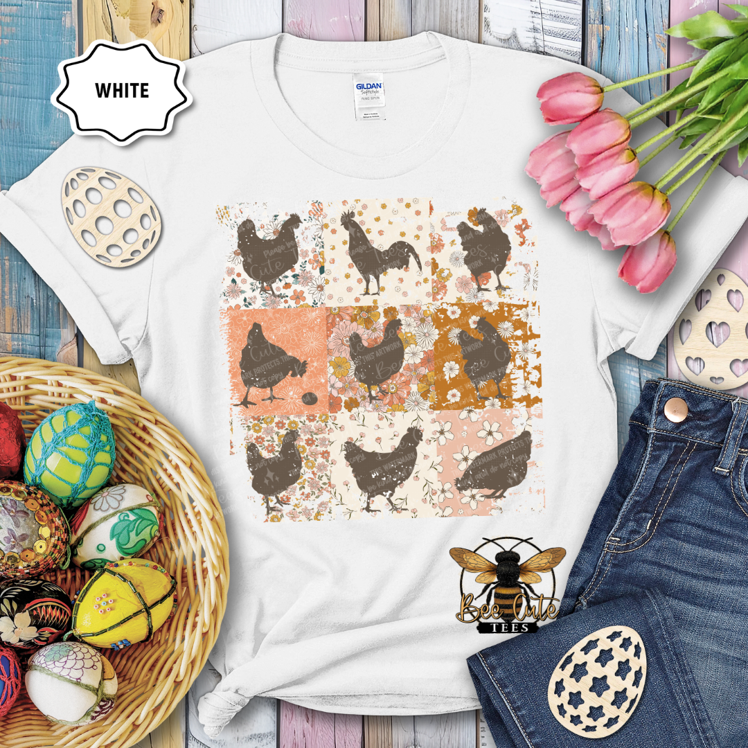 White t-shirt with chicken pattern, surrounded by Easter decorations on a wooden surface.