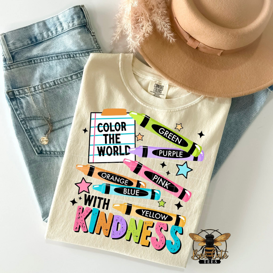 T-shirt with colorful text and crayon graphics, placed on jeans and a hat.