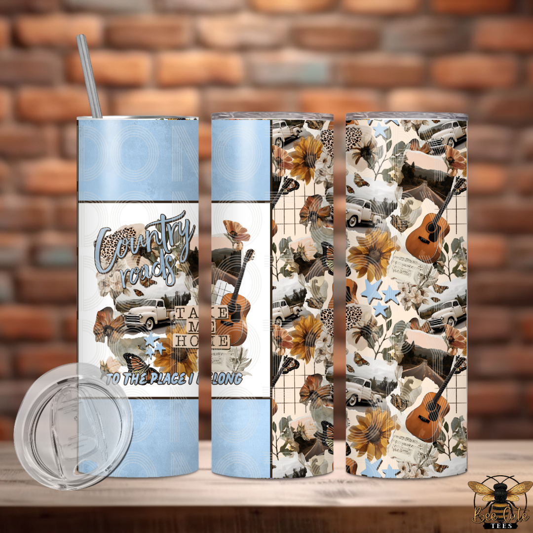 Tumbler with country-themed design featuring guitars, flowers, and text on a wooden surface with a brick wall background.