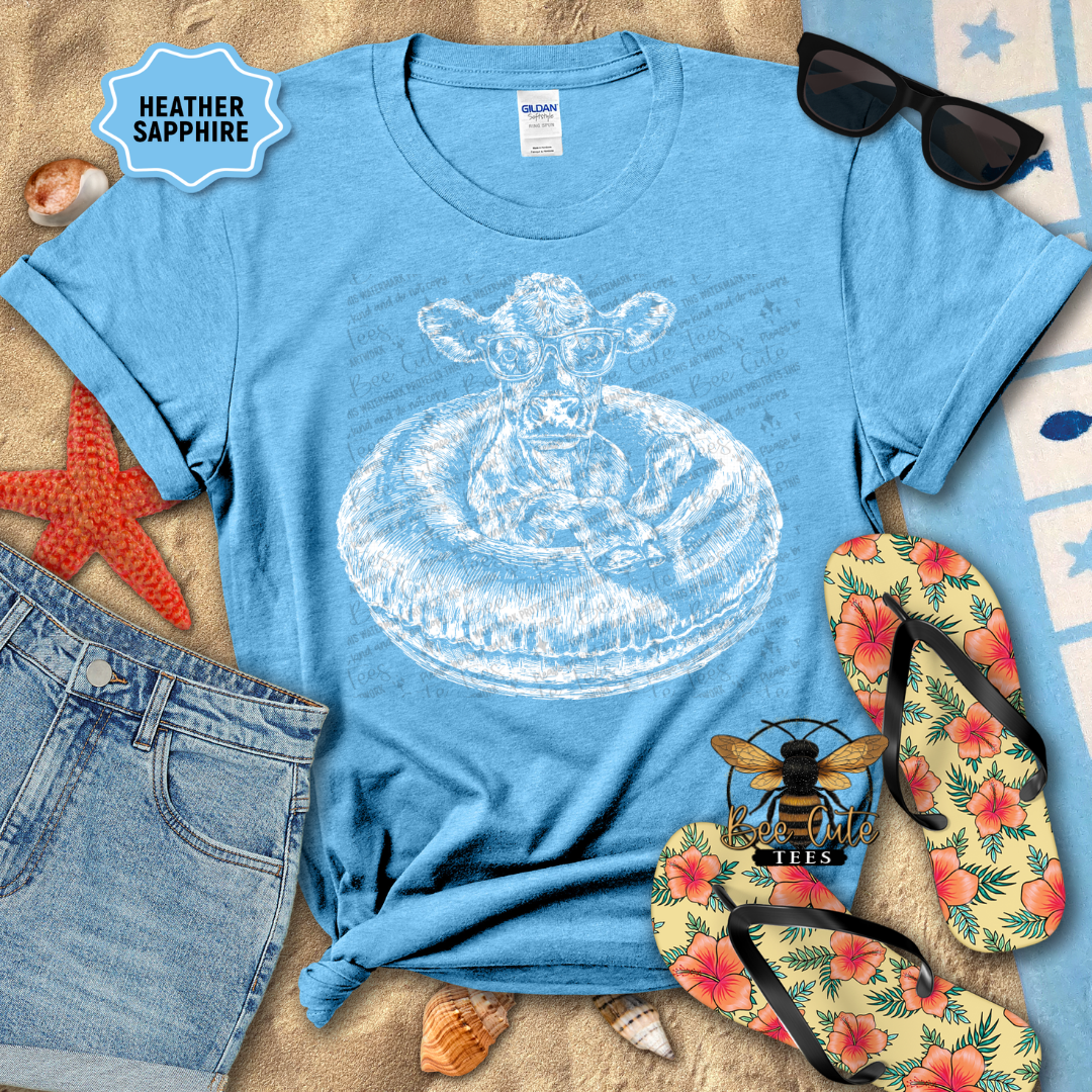 Blue t-shirt with a graphic design, sunglasses, flip-flops, and beach items on a sandy background.