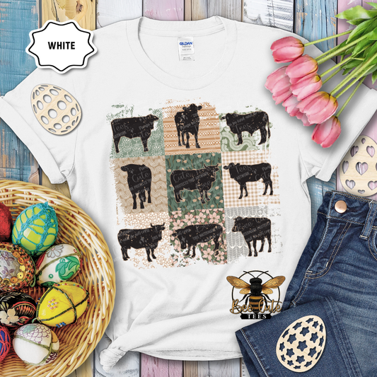 White t-shirt with cow pattern, surrounded by decorative items on a wooden surface.