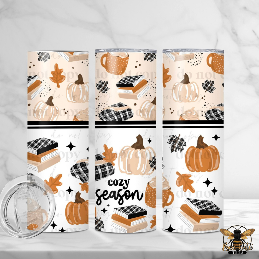 Three insulated tumblers with a fall-themed pattern of pumpkins, books, coffee cups, leaves, and stars, alongside a clear lid, displayed on a white marble background.