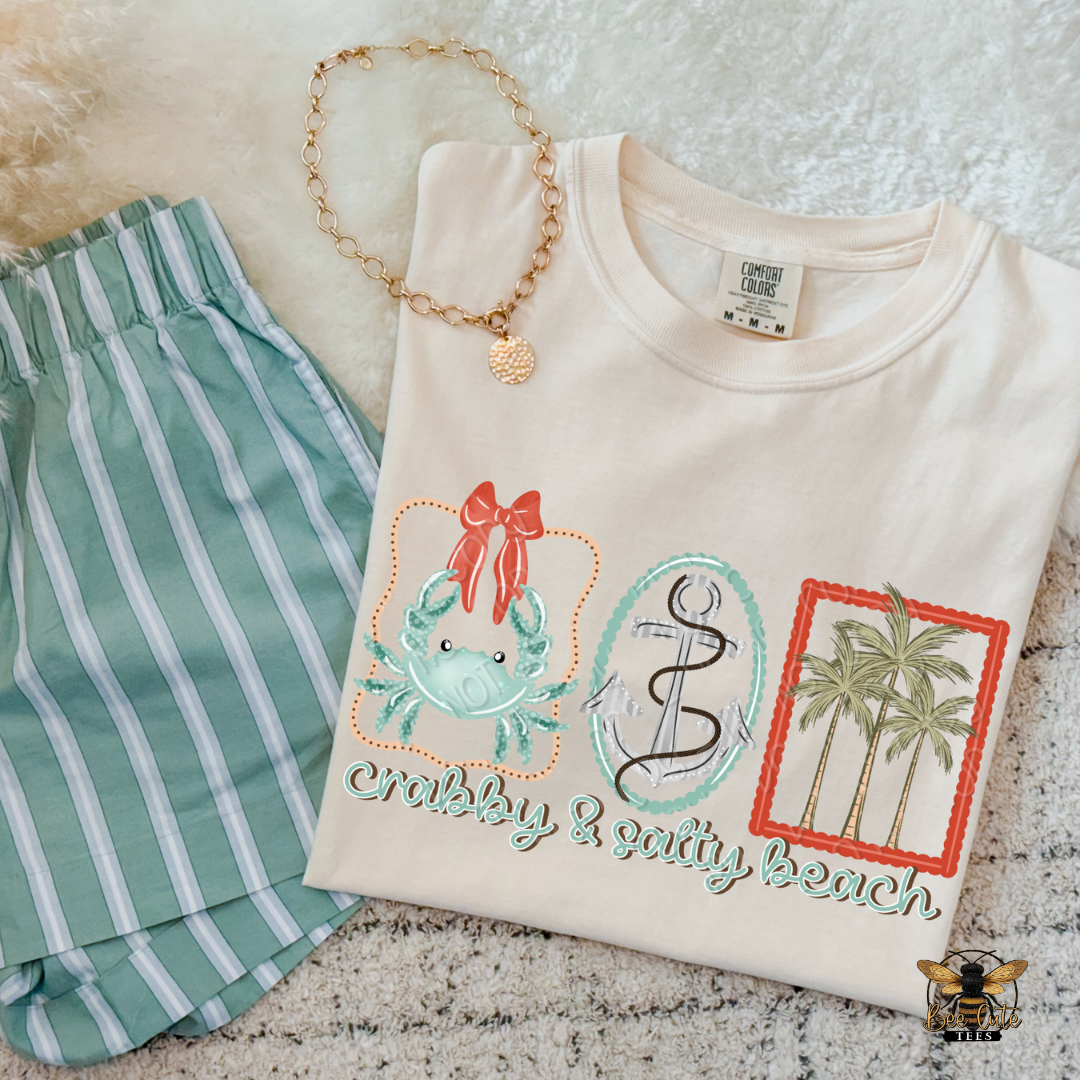 Beige t-shirt with beach-themed designs and green shorts on a textured surface