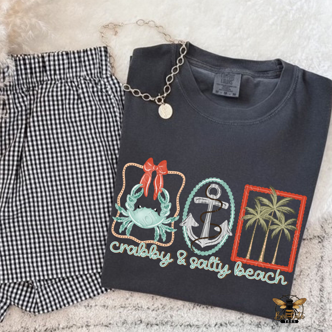 Black t-shirt with beach-themed design and checkered pants on a textured surface