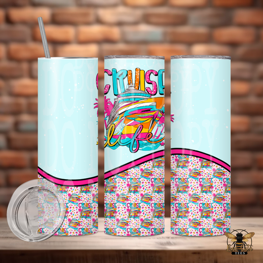 Colorful 20 oz tumbler featuring a vibrant cruise ship design, tropical accents, and “Cruise Life” themed artwork with pastel blue and pink details, displayed with a lid and metal straw against a rustic brick background.
