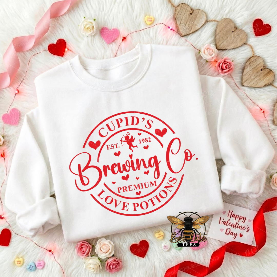 White sweatshirt with red 'Cupid's Brewing Co' text on a decorative background with flowers and hearts.