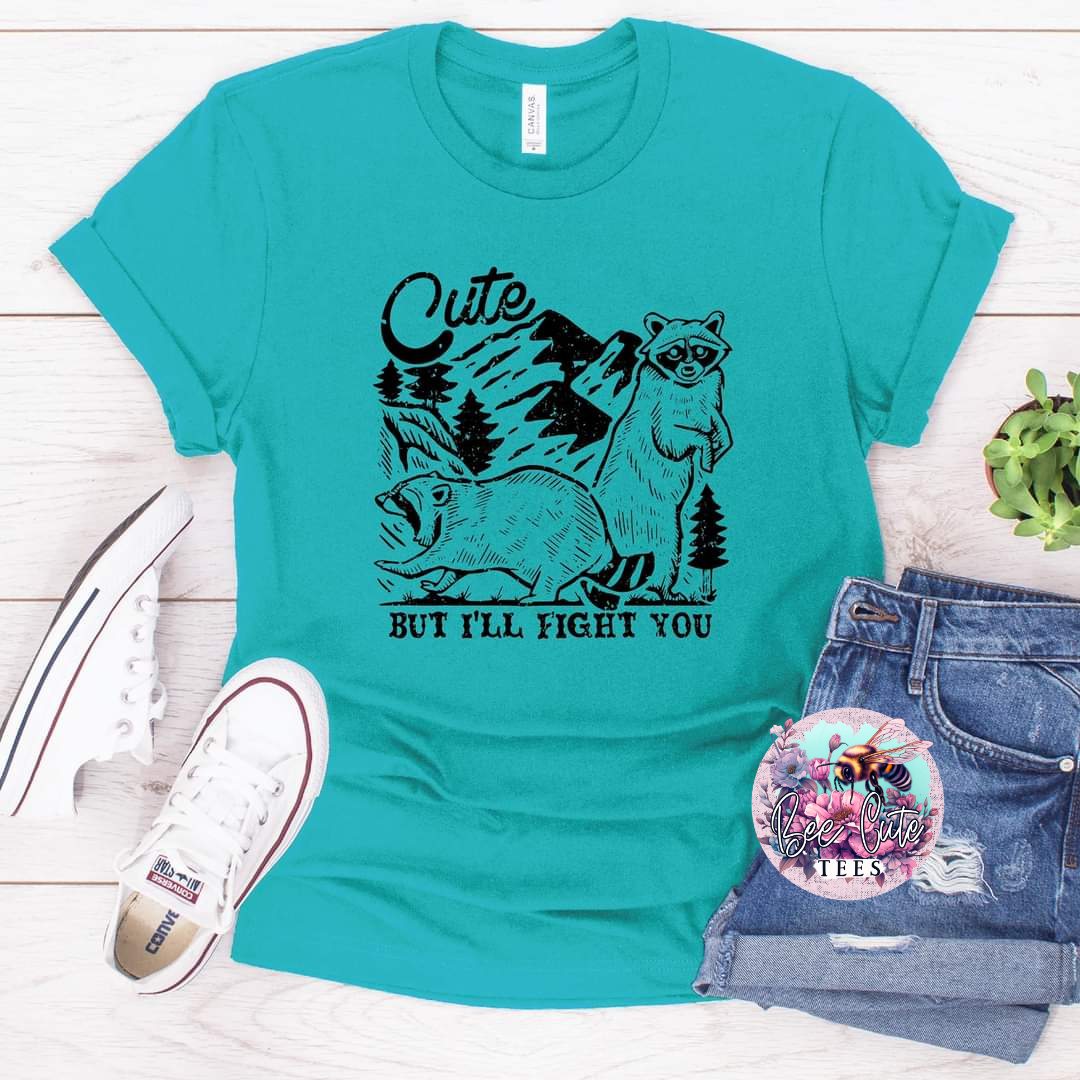 Turquoise t-shirt with raccoon graphic and text, paired with jeans and sneakers on a light wooden surface.