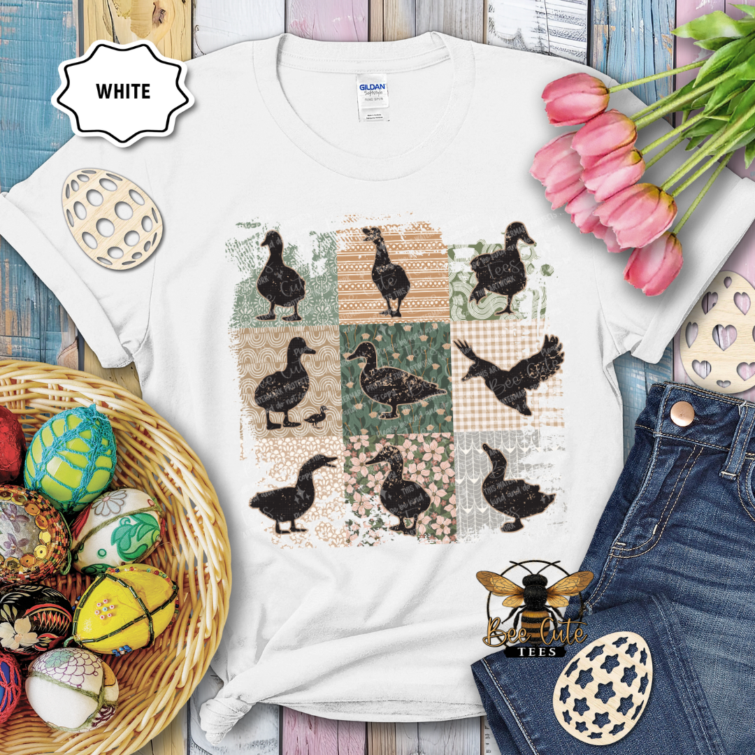 White t-shirt with duck pattern, surrounded by Easter decorations on a wooden surface.