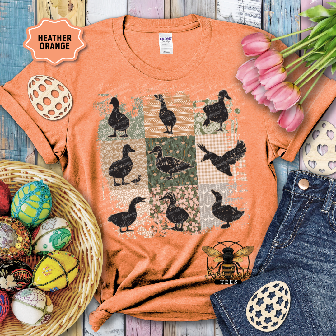 Orange t-shirt with duck pattern, surrounded by tulips and Easter decorations on a wooden surface.