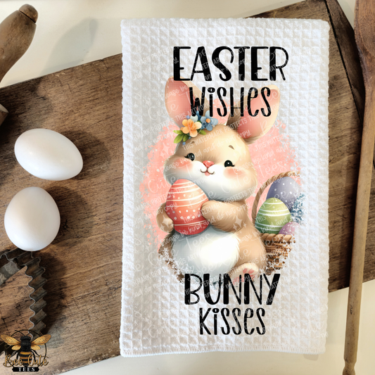 Easter-themed towel with a bunny holding an egg and text on a wooden surface with eggs.