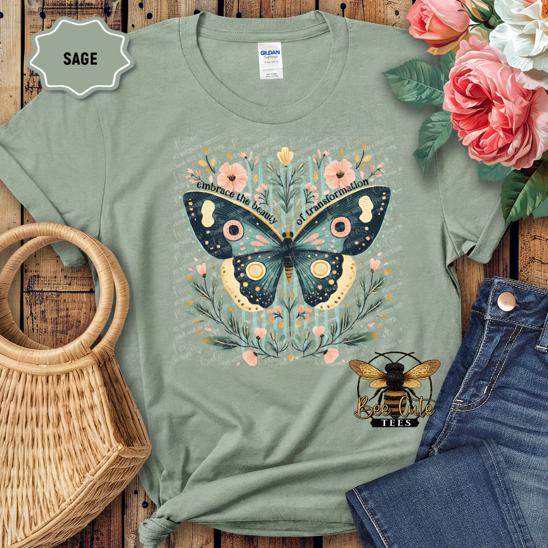 Sage green t-shirt with butterfly design on a wooden surface with flowers and jeans.