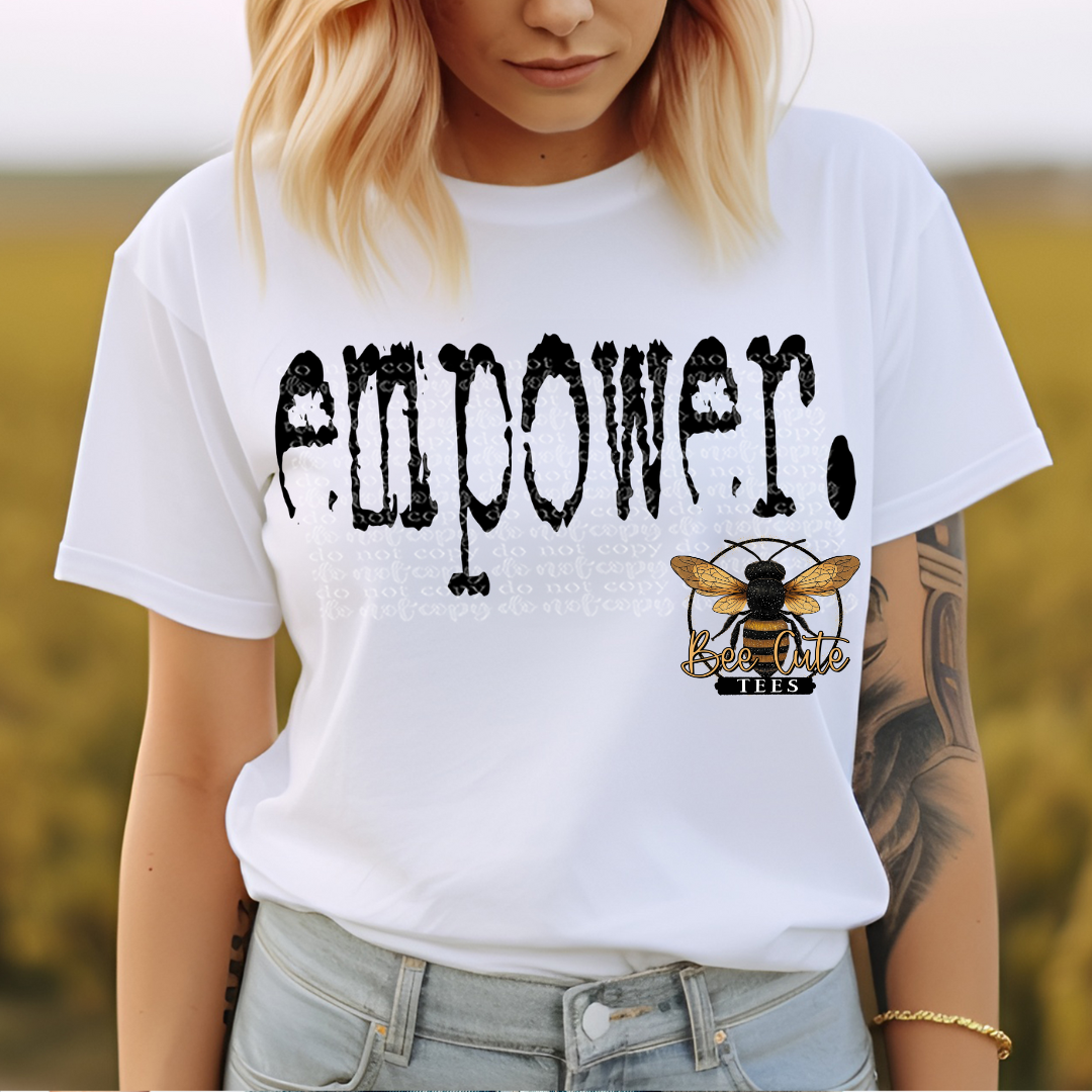 Person wearing a white t-shirt with 'EMPOWER' and a bee logo, standing outdoors.