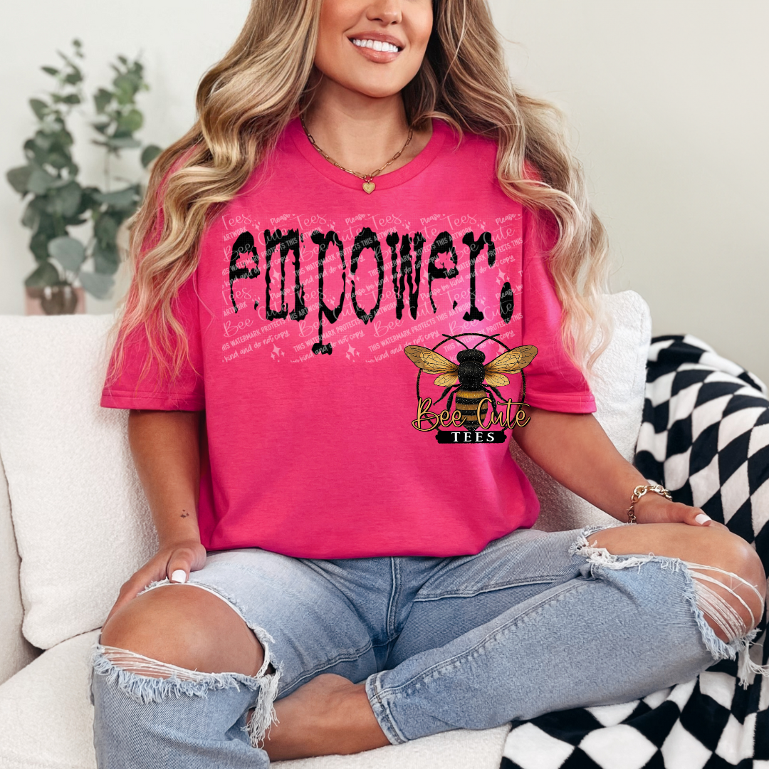 Person wearing a pink t-shirt with 'empower' and a bee logo, sitting on a couch.