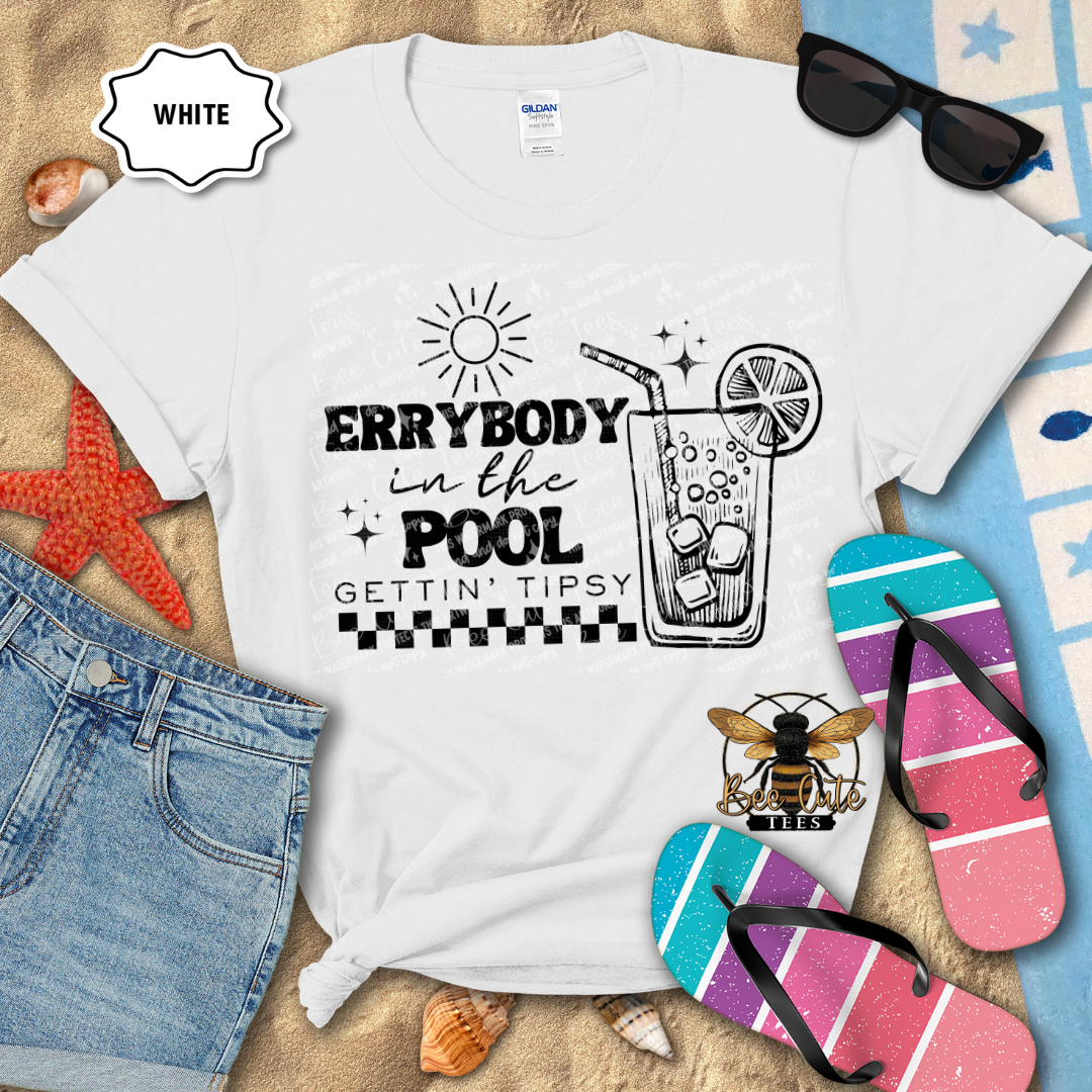White t-shirt with pool-themed design on a beach setting with sunglasses, flip-flops, and denim shorts.