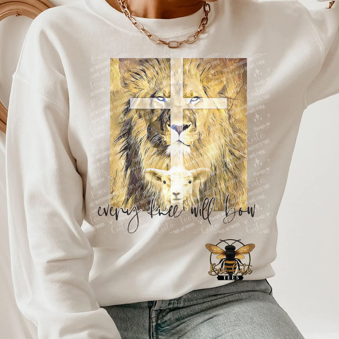 White sweatshirt with a graphic of a lion and lamb and a cross, with text 'every knee will bow' on a white background.