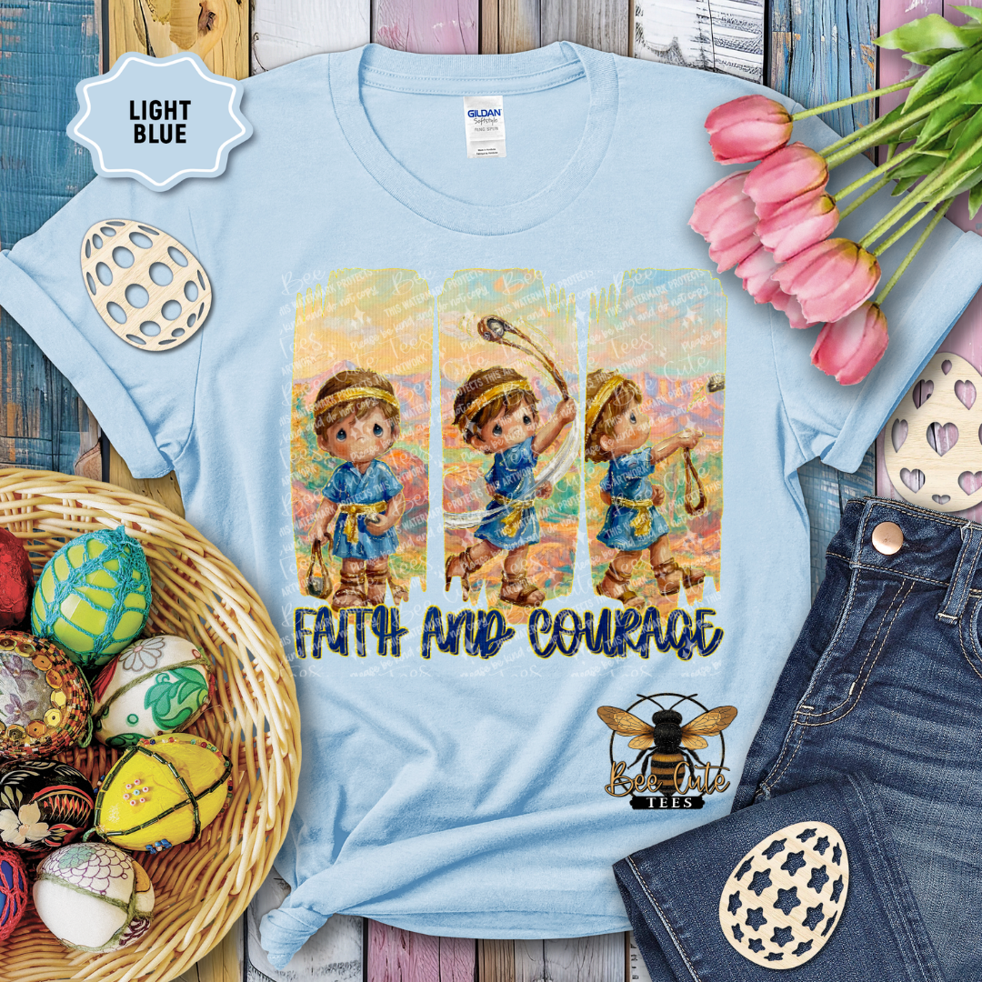 Light blue t-shirt with illustrated design of a boy playing sports, surrounded by decorative items on a wooden surface.