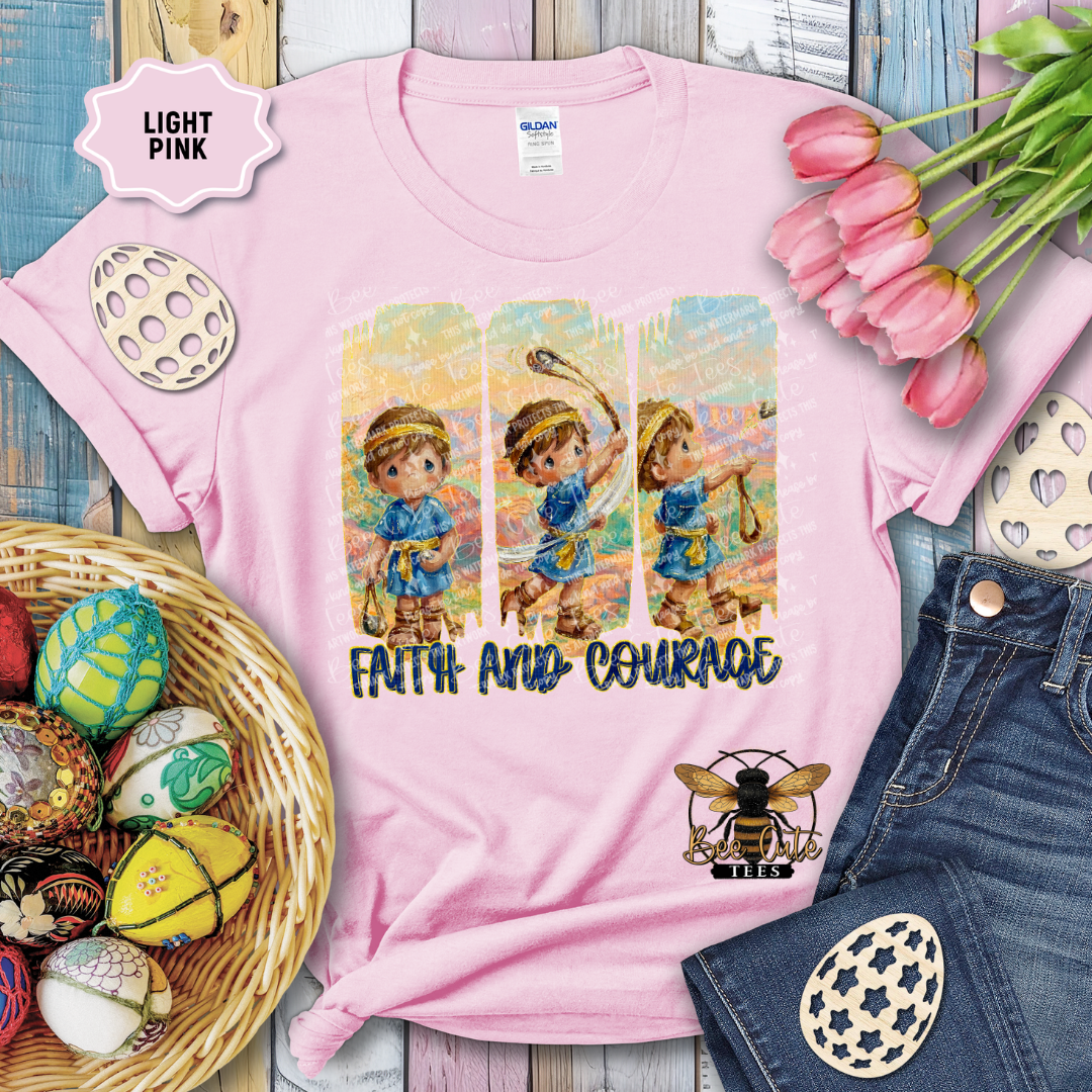 Light pink t-shirt with 'Faith and Courage' design, surrounded by Easter decorations on a wooden surface.