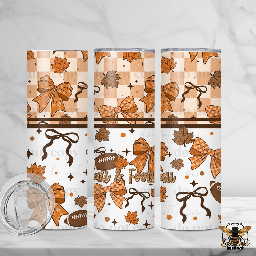 Three insulated tumblers with a fall-themed wrap design featuring orange and brown bows, maple leaves, footballs, stars, and a checkerboard pattern on a white marble background. A clear lid is shown in the lower left corner.