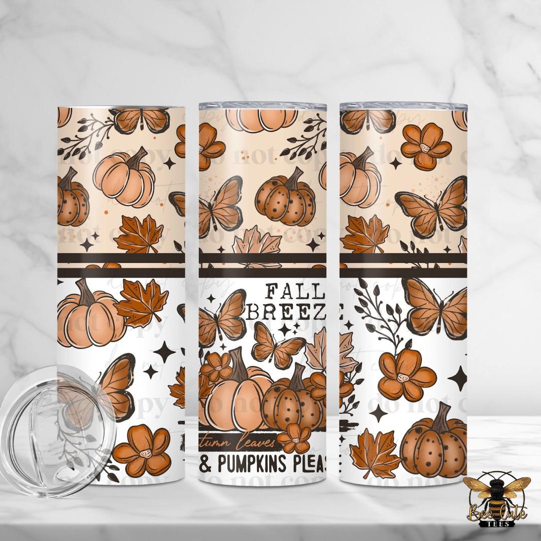 Three insulated tumblers with a fall-themed pattern of pumpkins, leaves, flowers, and butterflies, shown on a light marble surface with a clear lid in the foreground.