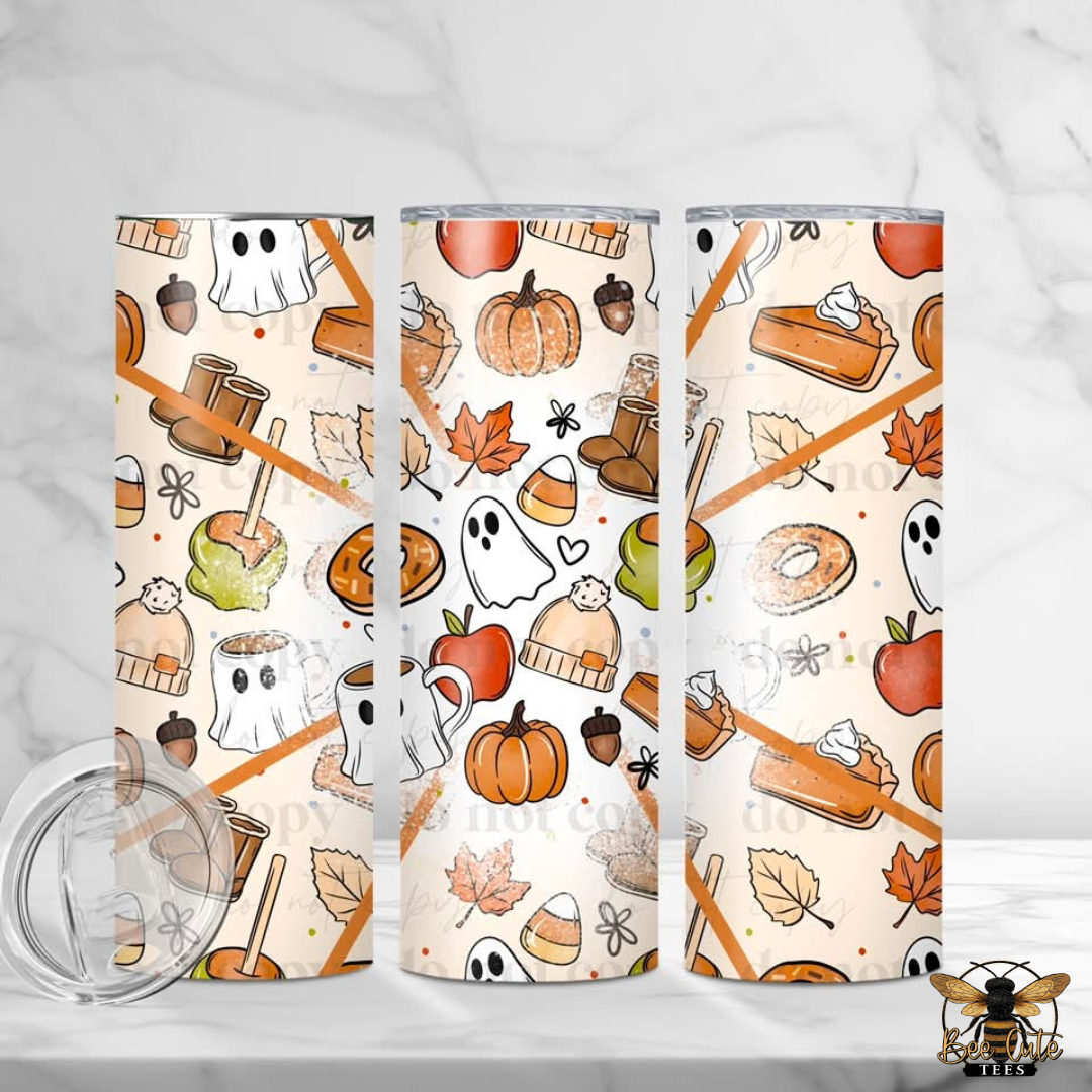 Three slim stainless steel tumblers with a Halloween-themed pattern featuring pumpkins, ghosts, acorns, candy corn, leaves, and treats on an off-white background. A clear lid is shown in the lower left on a light marble surface.