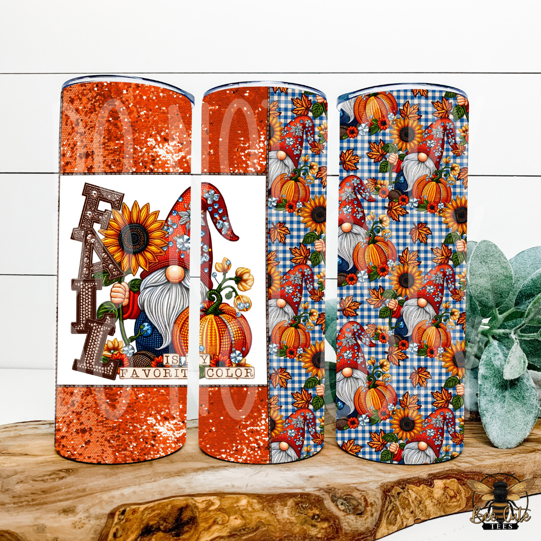 Three tall tumblers with autumn-themed wraparound prints are displayed on a rustic wood slice. The left tumbler features a glittery orange glitter pattern with a white band showing a gnome and sunflower design, with the words 'FALL IS MY FAVORITE COLOR'.