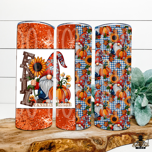 Three tall tumblers with autumn-themed wraparound prints are displayed on a rustic wood slice. The left tumbler features a glittery orange glitter pattern with a white band showing a gnome and sunflower design, with the words 'FALL IS MY FAVORITE COLOR'.