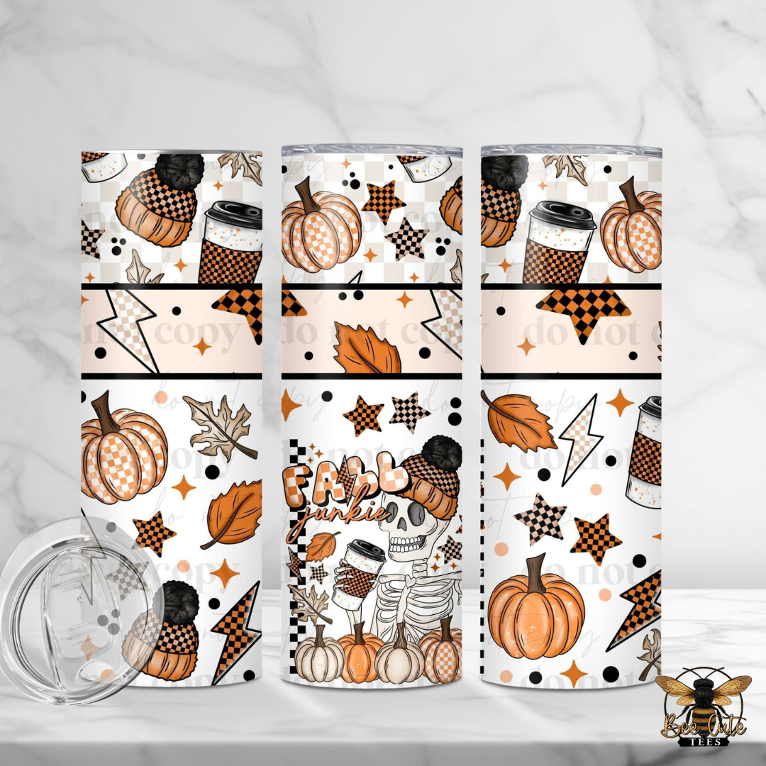 Three views of a skinny tumbler with a fall-themed 'Frostpunk' pattern, featuring pumpkins, skeleton characters, coffee cups, stars, and leaves on a white background. A clear lid is shown in the bottom left corner on a white marble surface.