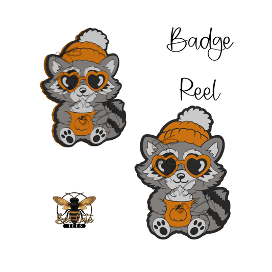 Two cartoon raccoon badges wearing orange knit hats and heart-shaped sunglasses, each holding an orange pumpkin cup, shown on a white background with the text 'Badge Reel' and a small bee logo reading 'BEE'.