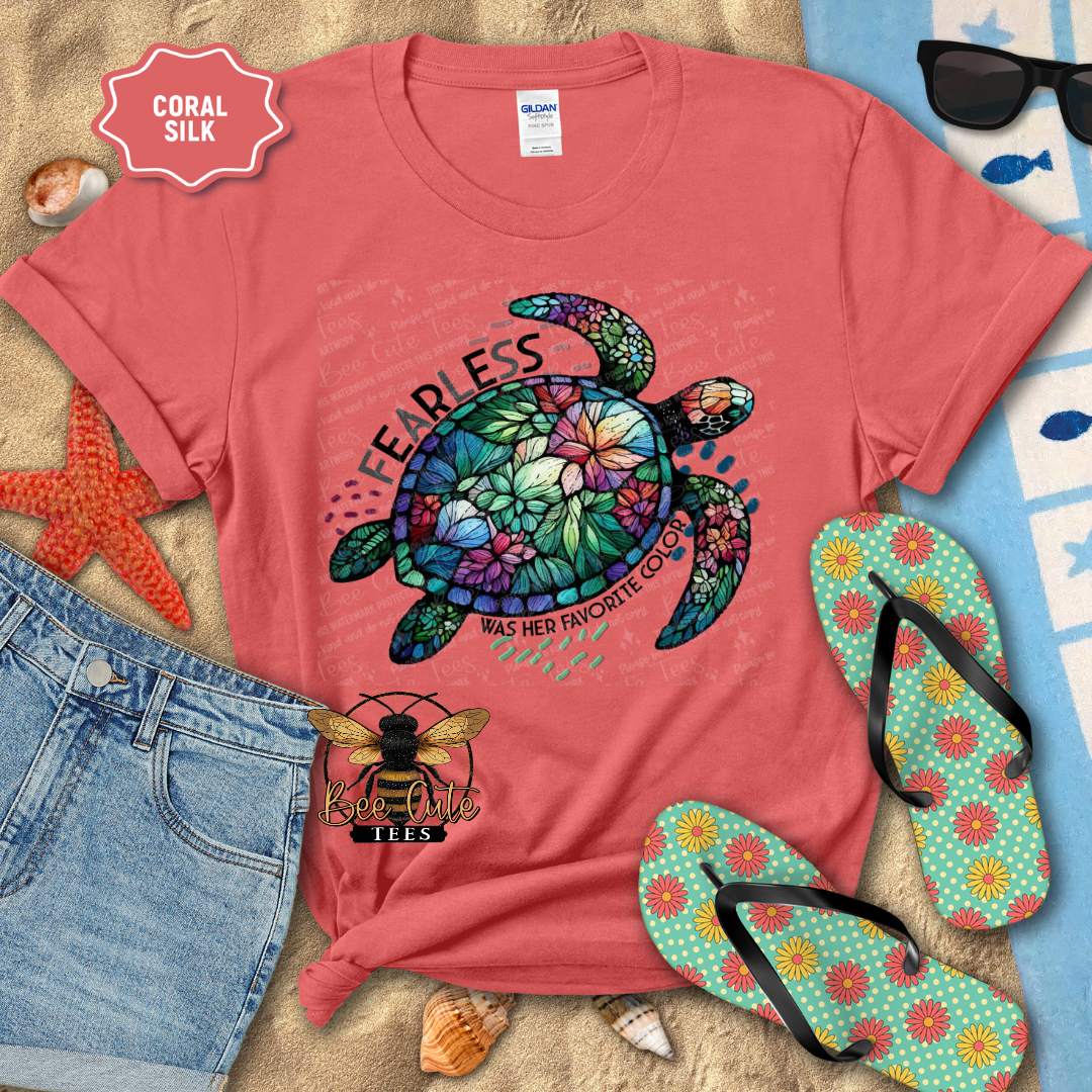 Coral t-shirt with colorful turtle design and 'Fearless' text, surrounded by beach items.