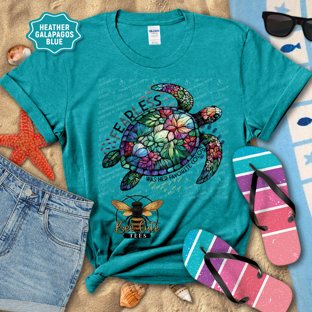 Teal t-shirt with a colorful turtle design on a beach-themed background with sunglasses, flip-flops, and starfish.