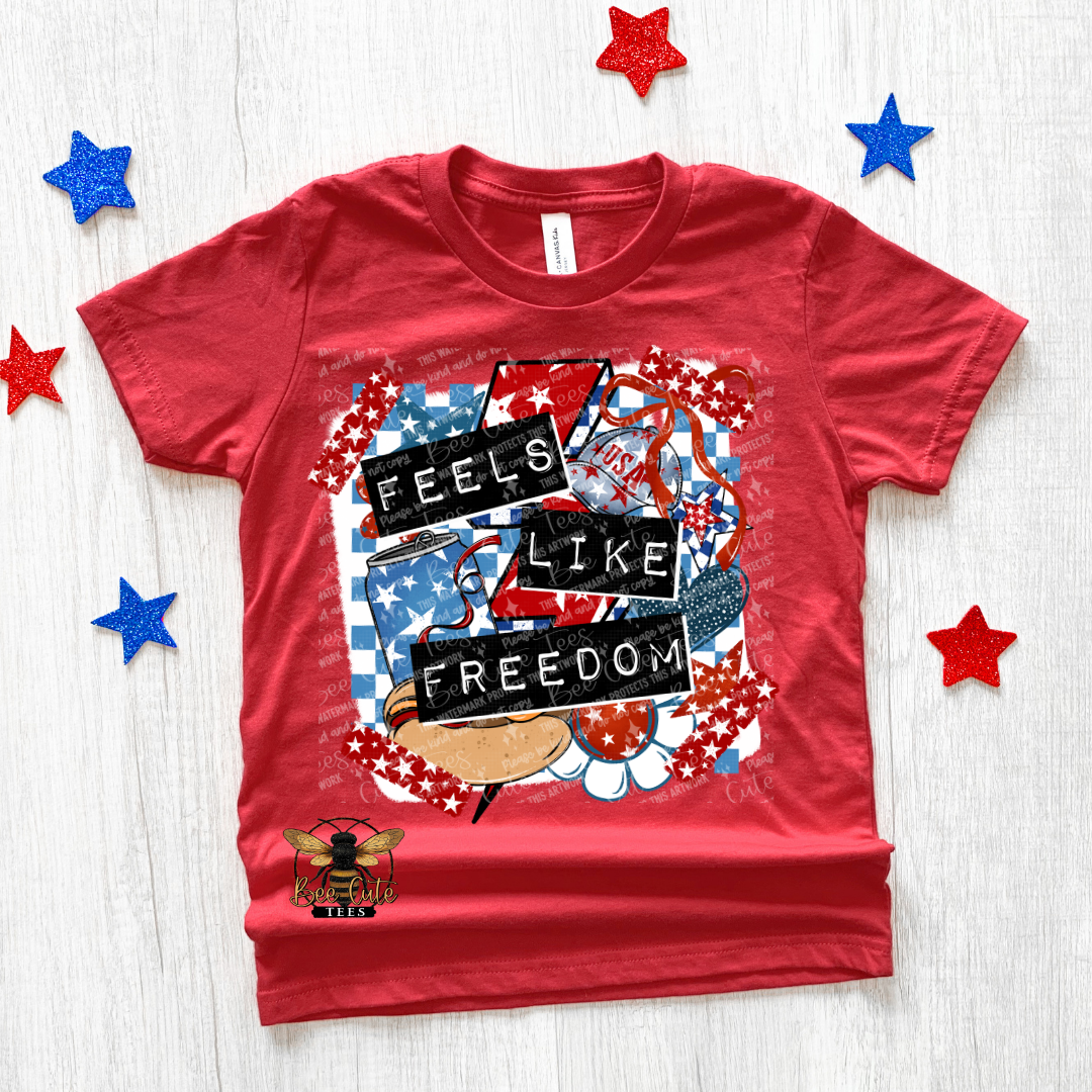 Red t-shirt with 'Feels Like Freedom' graphic design on a white background with decorative stars.