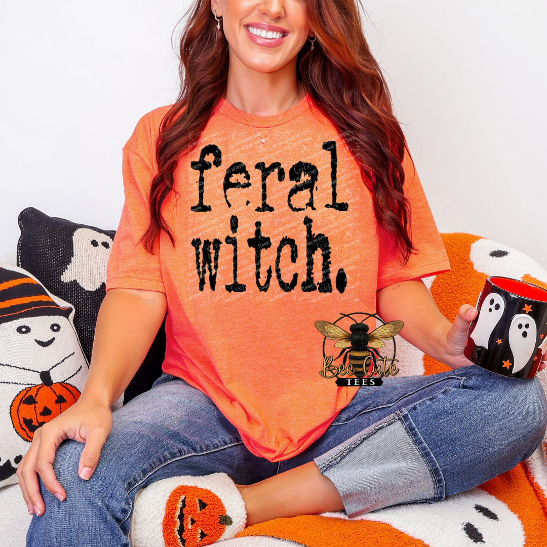 Person wearing an orange 'feral witch' shirt sitting on Halloween-themed pillows with a mug.