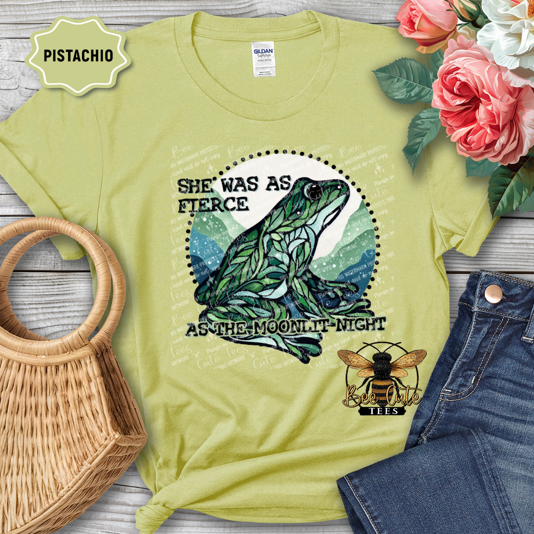 Pistachio green t-shirt with frog graphic and text, surrounded by flowers and denim jeans on a wooden surface.