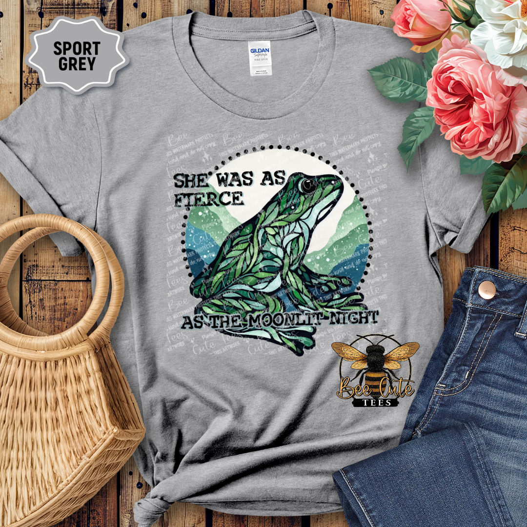 Gray t-shirt with a frog graphic and text on a wooden surface with flowers and jeans.