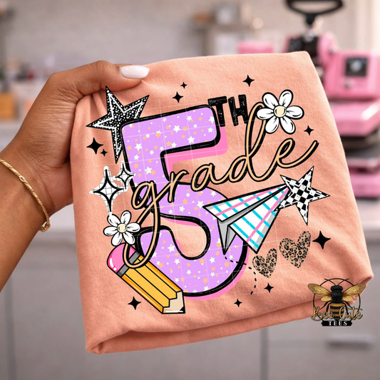 Folded orange shirt with '5th Grade' design held by a hand, with a blurred background.