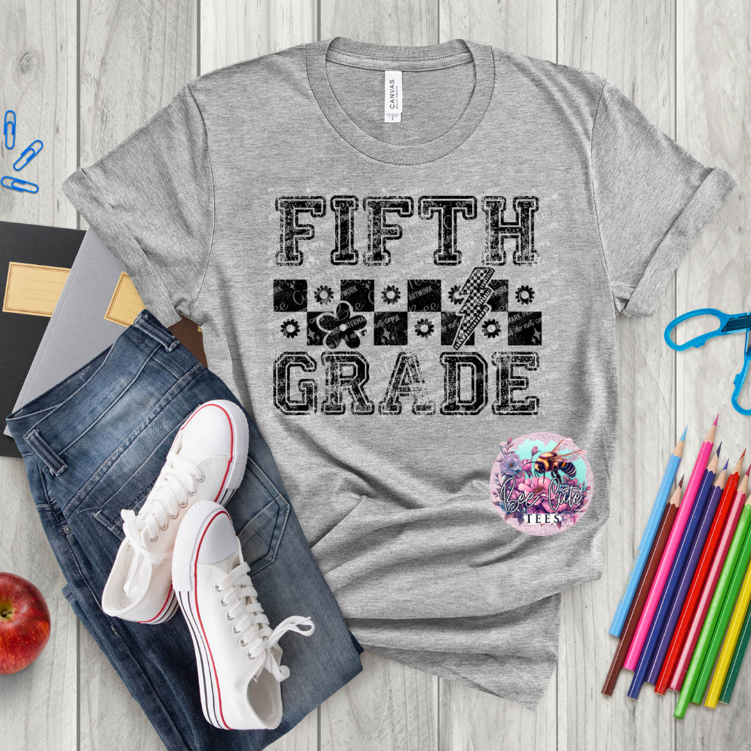 Grey t-shirt with 'Fifth Grade' text on a wooden surface with jeans, sneakers, and school supplies.