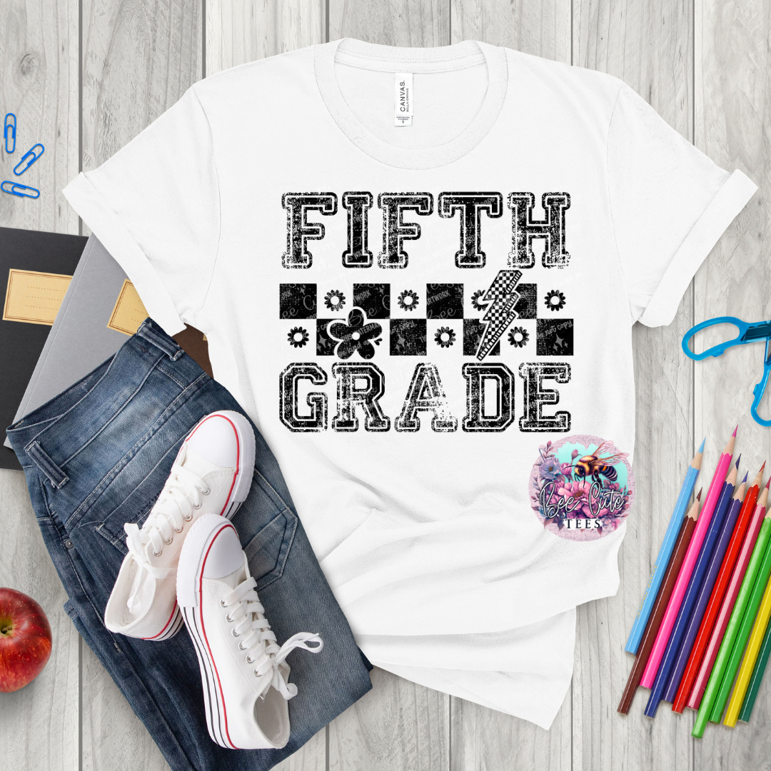 White t-shirt with 'Fifth Grade' text on a wooden surface with jeans, sneakers, and stationery items.