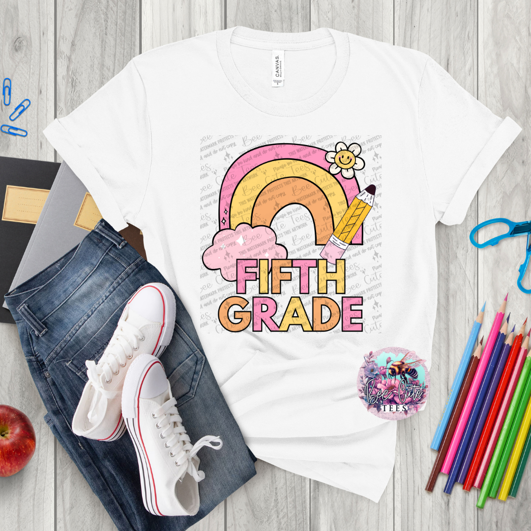 White t-shirt with 'Fifth Grade' design on a wooden surface with jeans, sneakers, and colorful pencils.