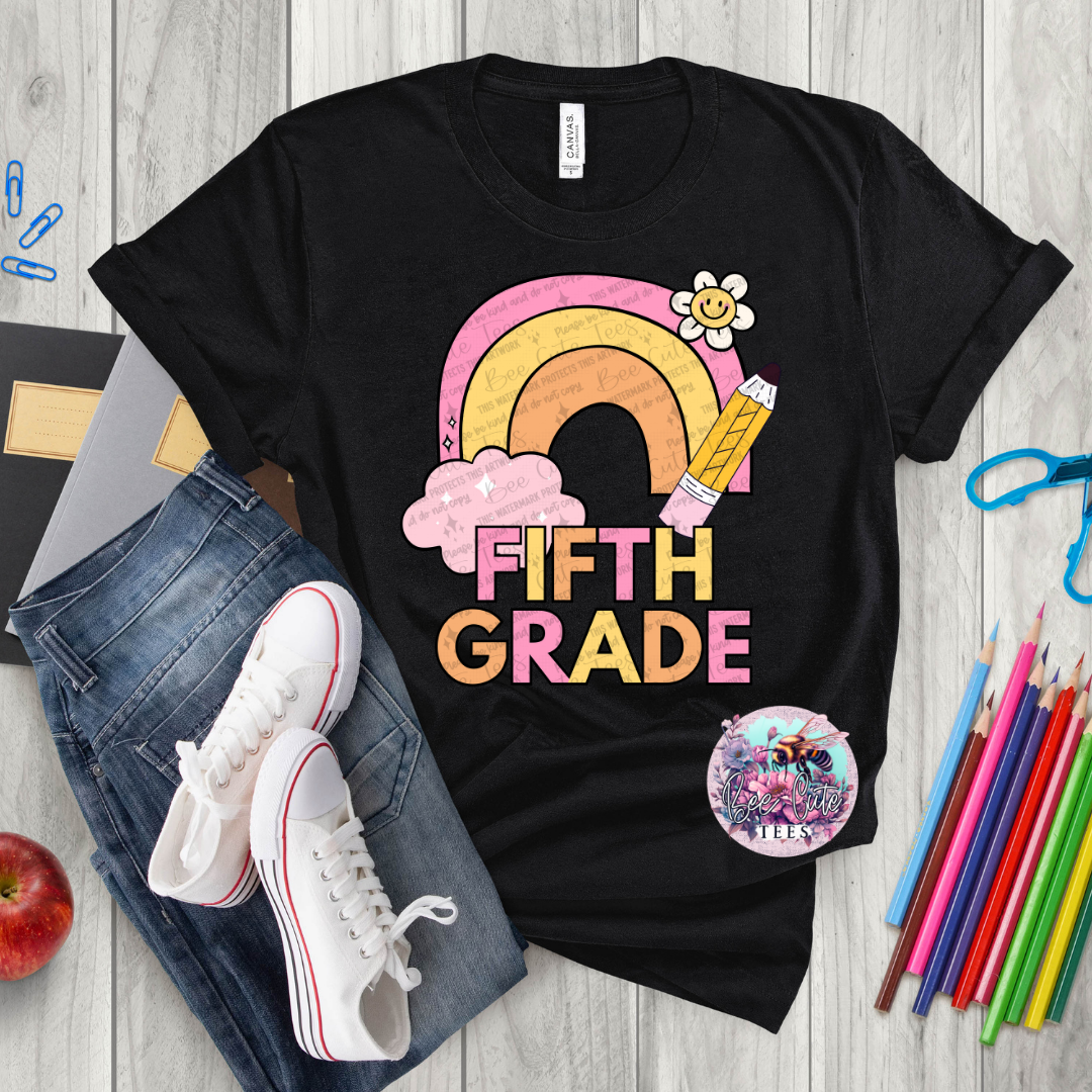 Black t-shirt with 'Fifth Grade' design on a wooden surface with school supplies.
