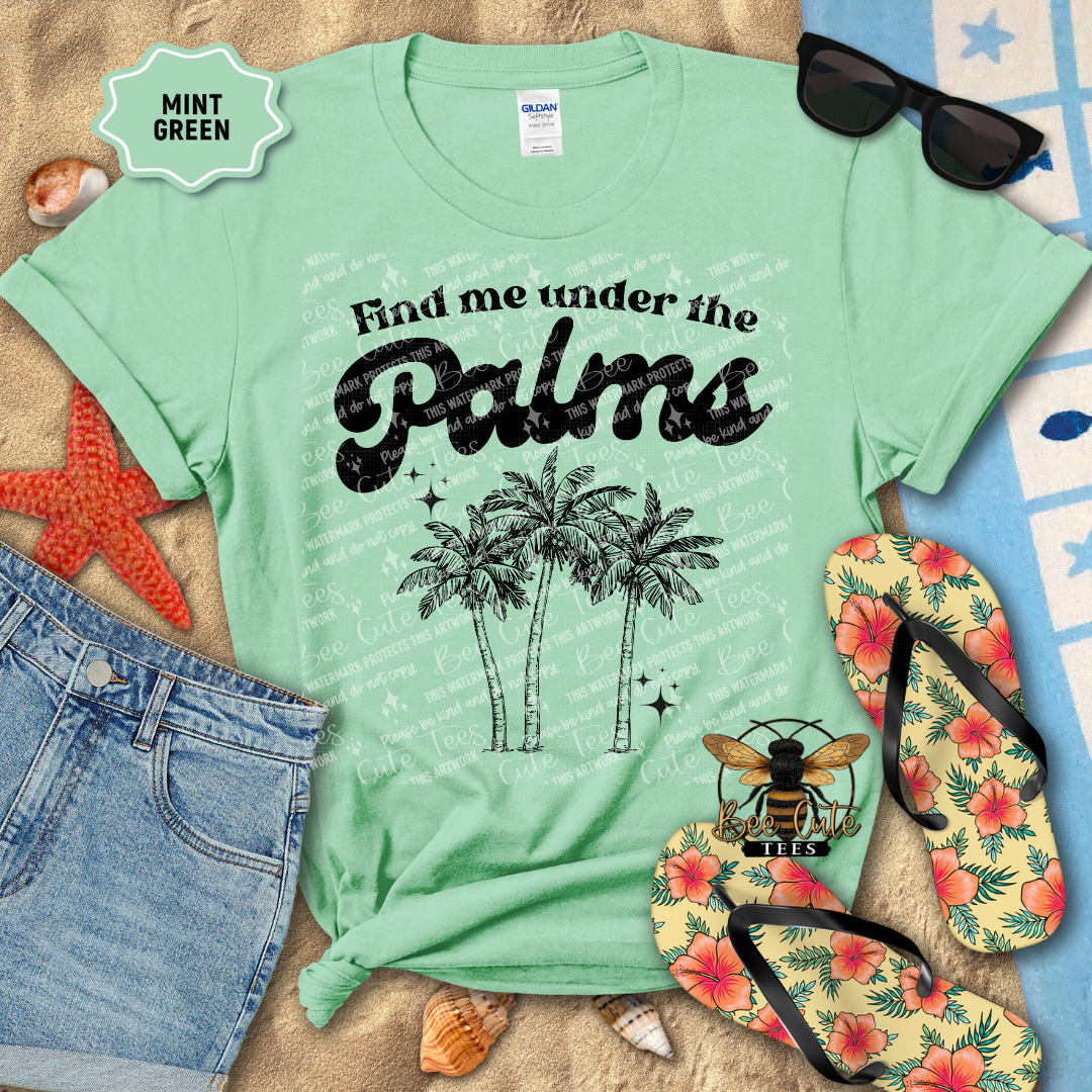 Mint green t-shirt with 'Find me under the Palms' design, sunglasses, flip-flops, and beach accessories on a sandy background.