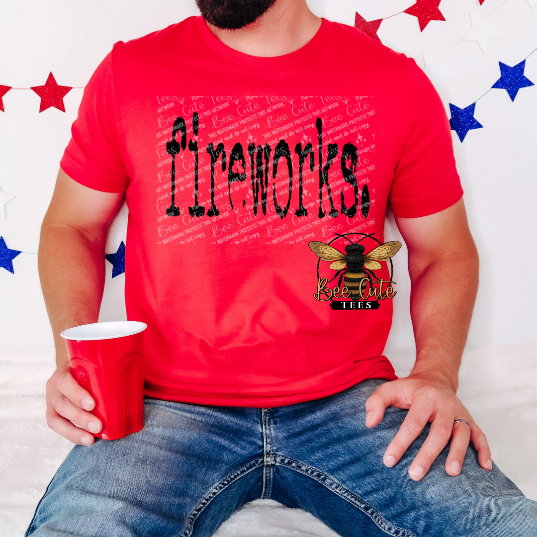 Red graphic t-shirt with distressed black text reading “Fireworks,” worn by a man sitting in denim jeans and holding a red cup, with red, white, and blue star decorations in the background and a Bee Cute Tees logo.
