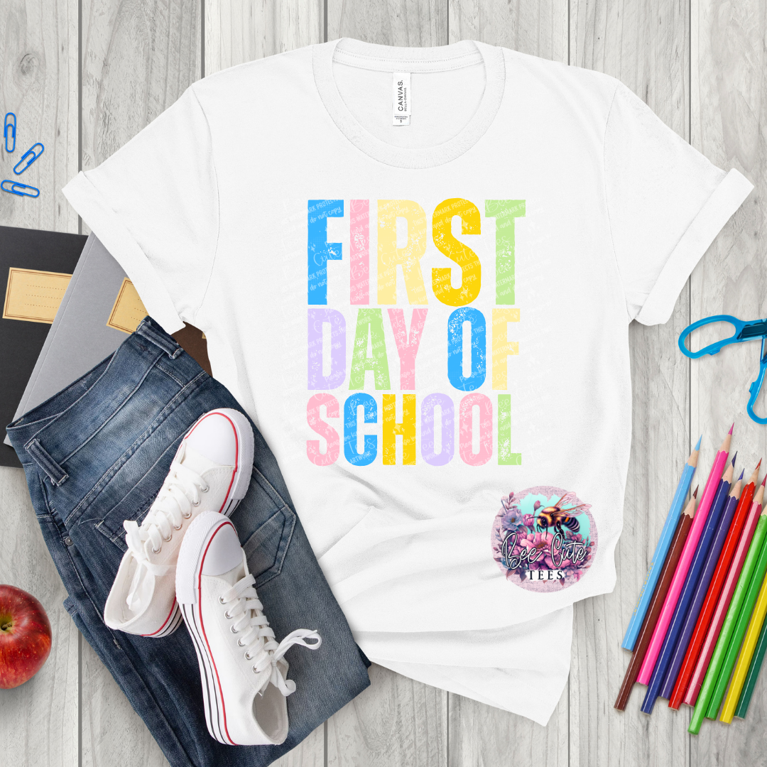 White t-shirt with 'First Day of School' text, jeans, sneakers, and school supplies on a wooden surface