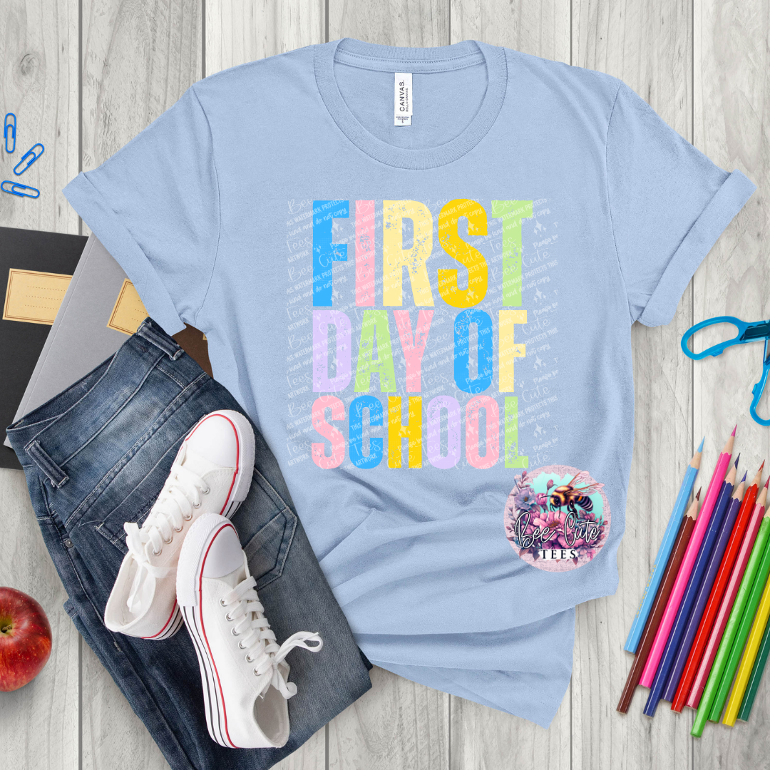 Light blue t-shirt with 'First Day of School' text, jeans, sneakers, and school supplies on a wooden surface.