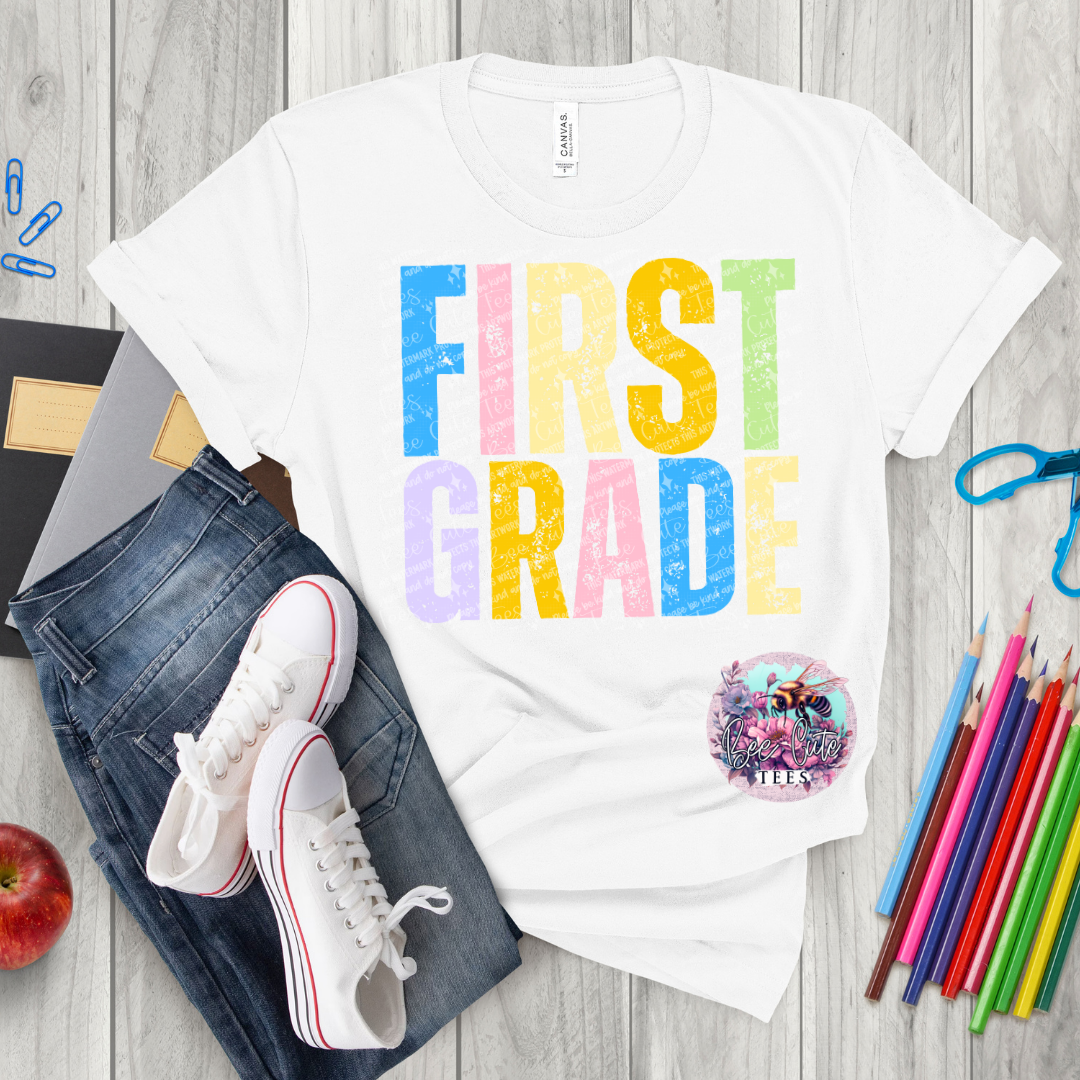 White t-shirt with 'FIRST GRADE' text on a wooden surface with jeans, sneakers, and school supplies.