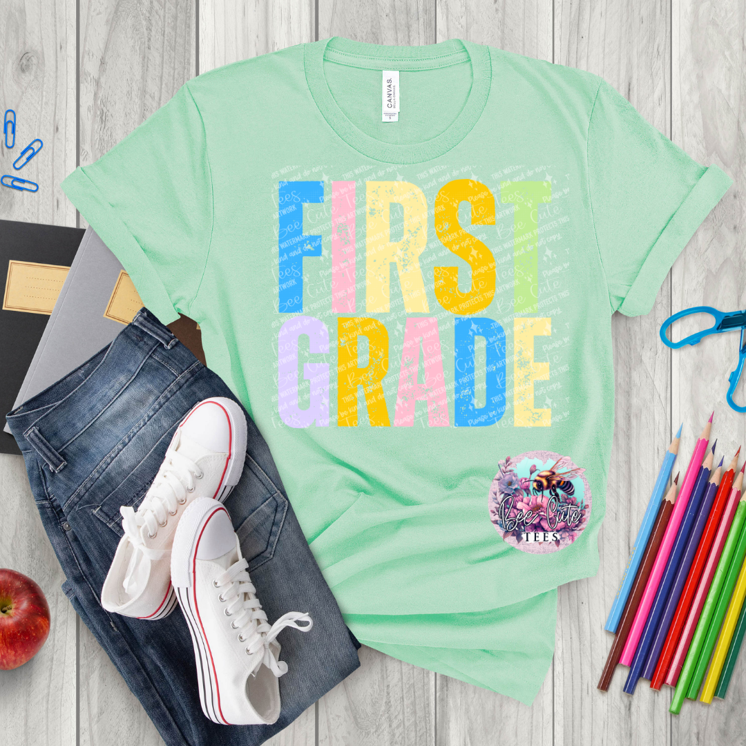 Light green t-shirt with 'FIRST GRADE' text, jeans, sneakers, and school supplies on a wooden surface