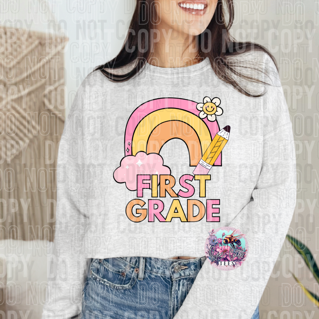 Person wearing a white sweatshirt with a colorful 'First Grade' design featuring a rainbow, pencil, and flower.