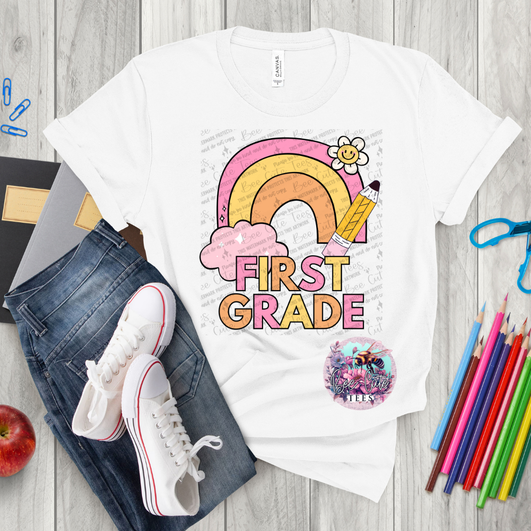 White t-shirt with 'First Grade' design on a wooden surface with school supplies.