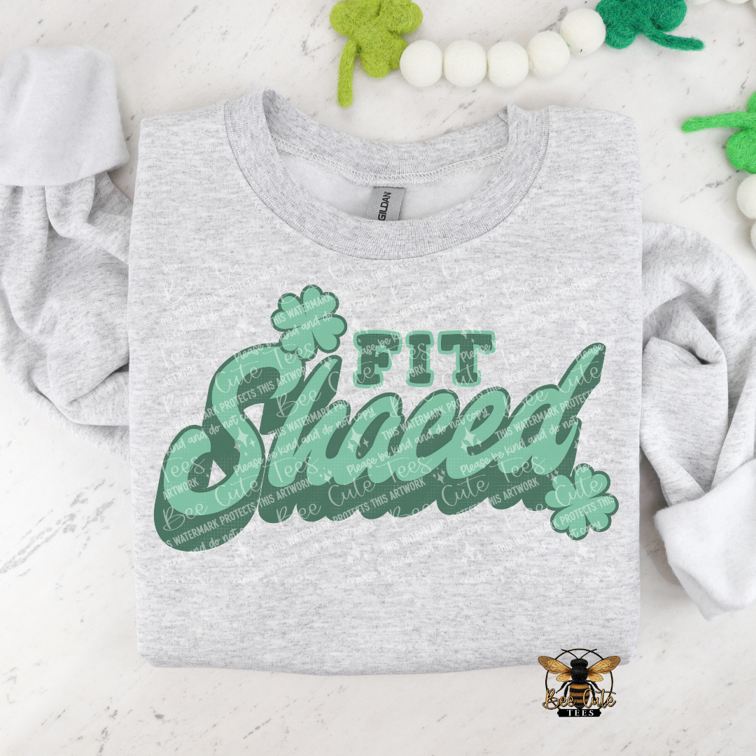 Gray t-shirt with green text and shamrock graphics on a white surface with decorative elements.