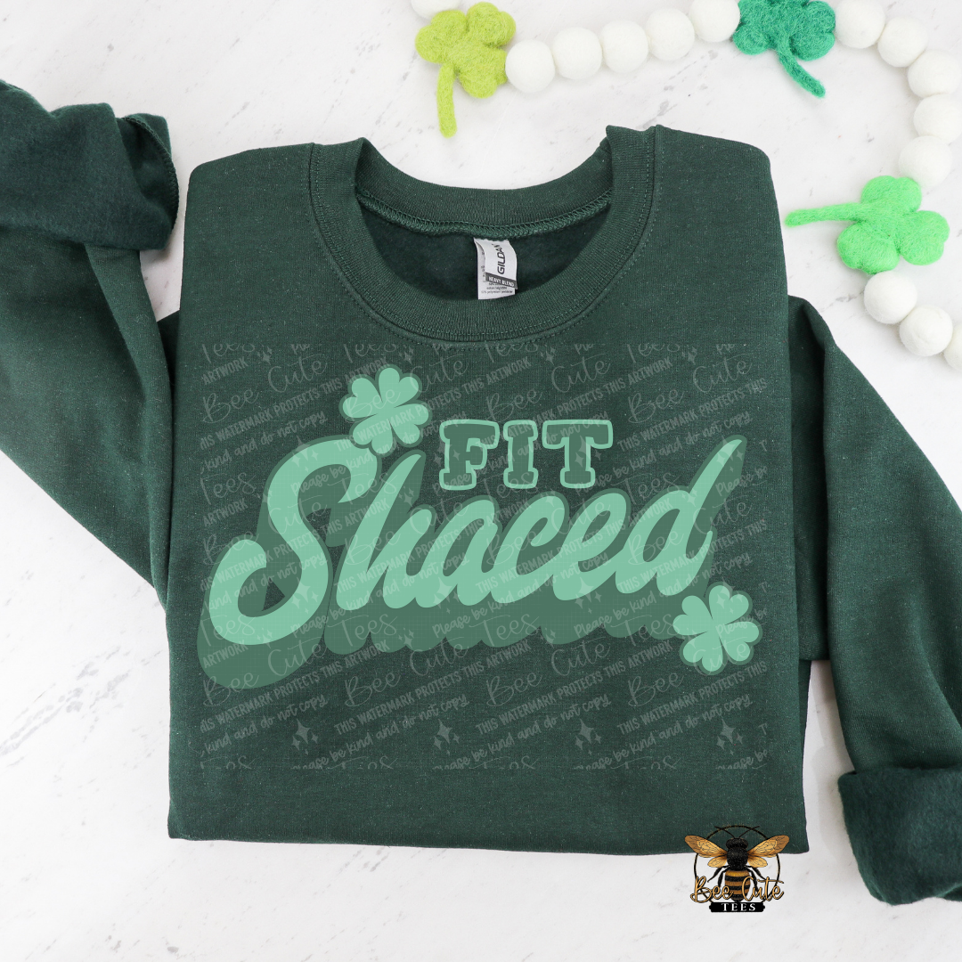 Green sweatshirt with 'Fit Shaced' text and shamrock designs on a white background with decorative elements.
